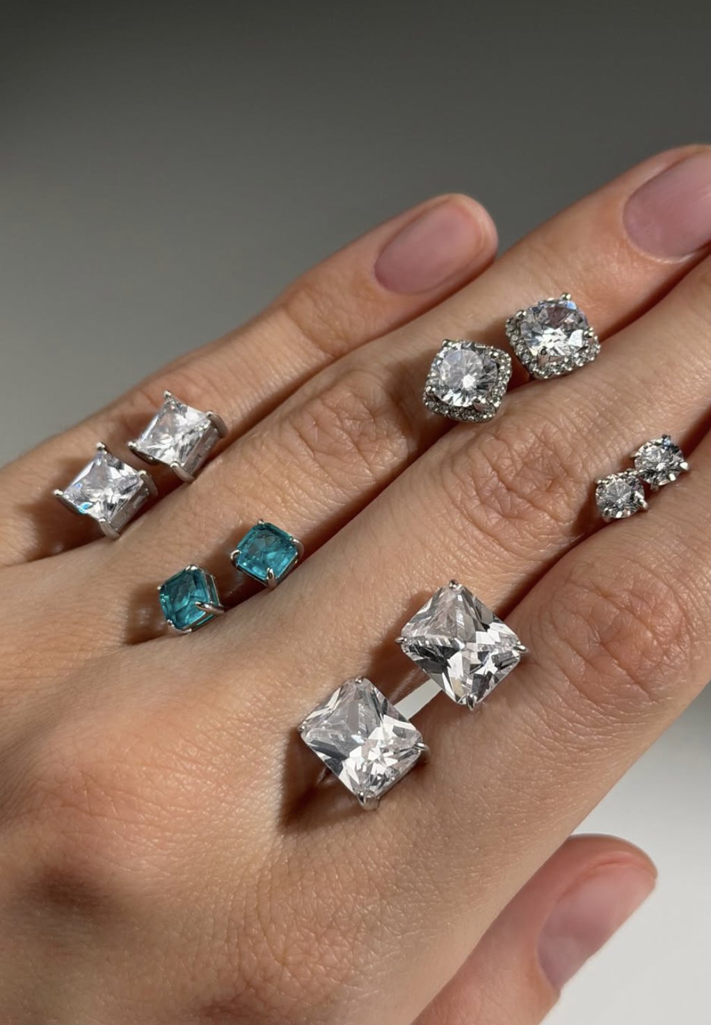 Clear and aqua stud earrings and rings shown on a hand